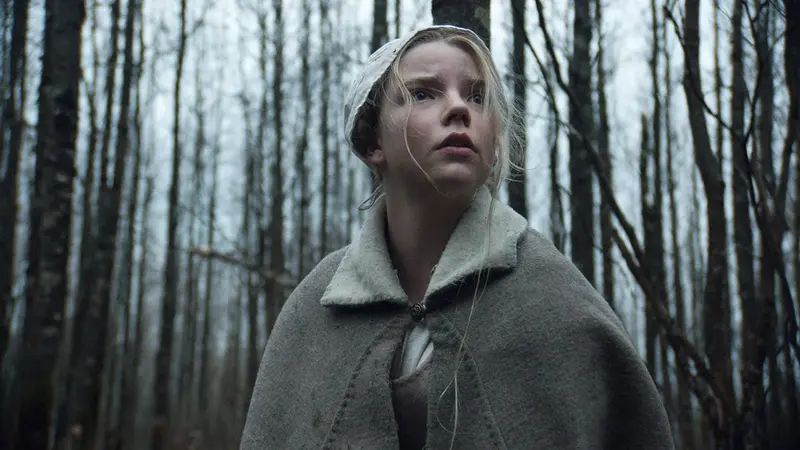 Anya Taylor-Joy as Thomasin standing in a dark forest in The Witch