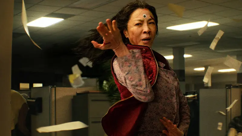 Michelle Yeoh in a fighting stance amid flying papers in an office in Everything Everywhere All at Once